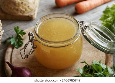 Homemade bone broth in a glass jar, with fresh vegetables