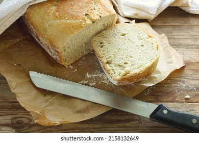 homemade bread with grains on a sheet of paper, piece is cut off with knife, white towel on wooden table, closeup