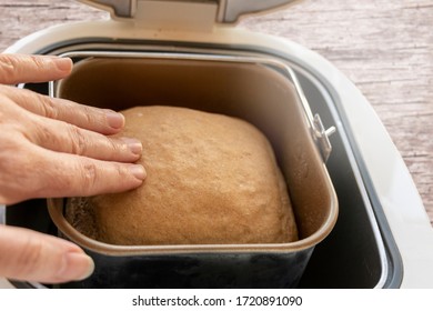 Homemade bread in the bread maker is checked by one hand. View from above.