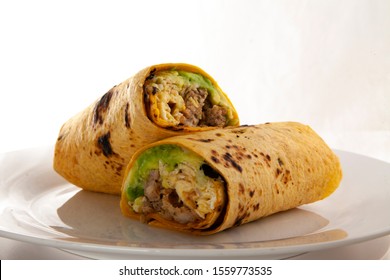 A Homemade Breakfast Burrito Turning On A White Plate With A White Background.  The Delicious Burrito Has Sausage, Egg, Cheese, And Avocado In It.