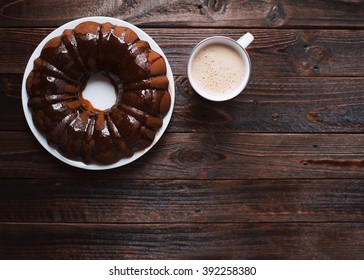 Homemade Bundt Cake With Chocolate Icing, Cup Of Hot Coffee On A Dark Wooden Table. Top View.