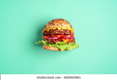 Homemade burger with double beef patties, cheese, and salad isolated on a green-mint background. Single hamburger side-view - Powered by Shutterstock