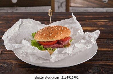 Homemade Burger Stuffed With Dried Red Fish, Tomato, Onion, Pickled Cucumber, Lettuce Leaves In Paper On A Plate Close-up. Fast Food. Horizontal Orientation, No People, Copy Space