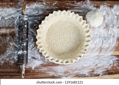 Homemade butter pie crust in pie plate with fluted pinched edge, rolling pin and extra ball of dough over floured rustic wooden background. Crust has been perforated with fork and ready for baking. - Shutterstock ID 1191681121