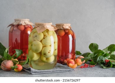 Homemade canned apple and cherry compote in large glass jars on gray tabletop. Save fall and summer harvest.