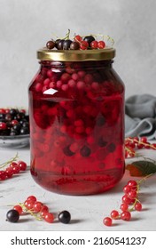 Homemade canned compote with black and red currants in glass jar on a light gray background