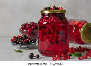 Homemade canned compote with cherries and currants in two jars on a light gray background.