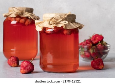 Homemade canned compote with strawberries in two jars on light gray background