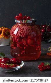 Homemade canned compote with sweet cherries and red currants in glass jar on dark gray background, Vertical format