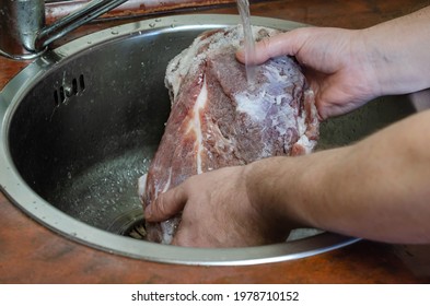 Homemade Capicola (coppa). Dry-cured pork loin step-by-step recipe. Man washes salt off a piece of pork. His hands hold the marinated meat in the sink under running water. Traditional Italian cuisine