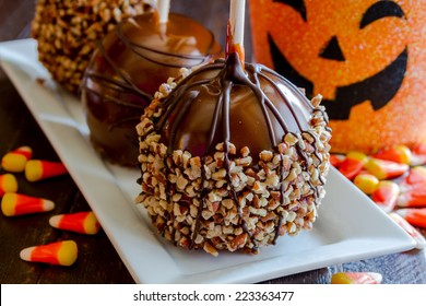 Homemade Caramel Apples With Nuts And Chocolate Drizzle Sitting On White Plate With Halloween Pumpkin Bucket And Candy Corn