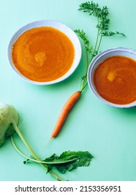 Homemade carrot soup in a bowl with raw carrot on green background