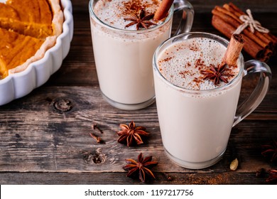 Homemade Chai Tea Latte with anise and cinnamon stick in glass mugs with pumpkin pie on wooden rustic background