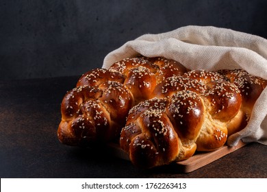 Homemade Challah bread with white cover, Jewish cuisine. Main ingredients are eggs, white flour, water, sugar, salt and yeast. Decorated with sesame and poppy seeds. Dark background.