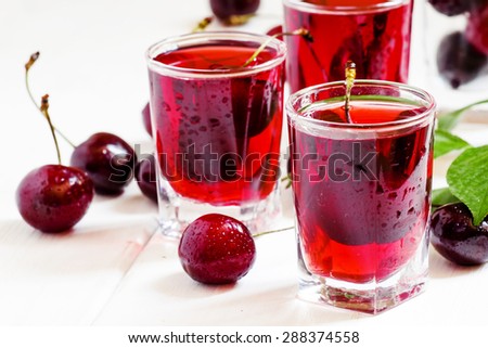 Homemade cherry liqueur and fresh cherries on white wooden background, selective focus