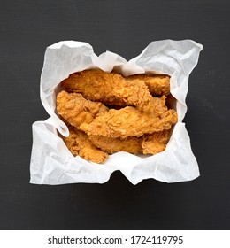 Homemade Chicken Fingers In Paper Box On A Black Surface, Top View. Flat Lay, Overhead, From Above. Close-up.