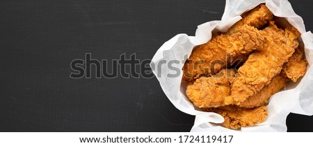 Homemade chicken fingers in paper box on a black background, top view. Flat lay, overhead, from above. Space for text.
