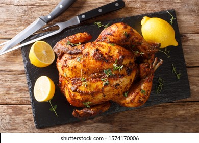 Homemade chicken rotisserie with thyme, lemon closeup on a slate board on the table. Horizontal top view from above