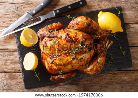 Homemade chicken rotisserie with thyme, lemon closeup on a slate board on the table. Horizontal top view from above