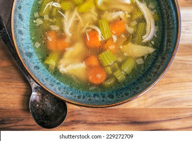 Homemade Chicken Soup In A Turquoise Bowl With An Antique Soup Spoon On A Wooden Table. 