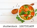 Homemade chicken vegetable soup, overhead view on a white wood background