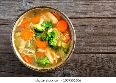 Homemade chicken vegetable soup, overhead, close up view on an old wood background