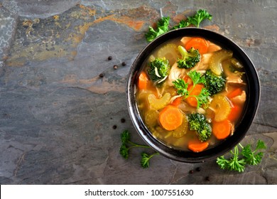Homemade chicken vegetable soup, overhead view on a dark slate background