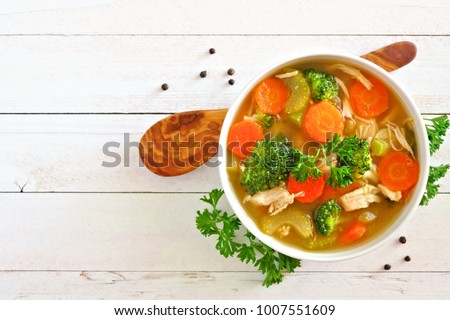 Homemade chicken vegetable soup, overhead view on a white wood background