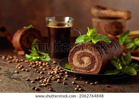 Homemade chocolate cake with mint and a mug of black coffee on a brown table.