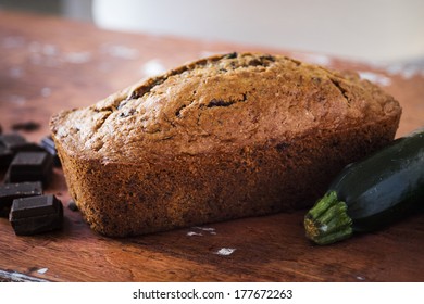 Homemade chocolate zucchini bread sitting on a wooden table with chocolate chunks and a zucchini