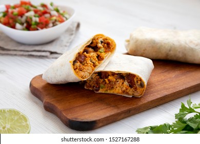 Homemade chorizo breakfast burritos on a rustic wooden board on a white wooden surface, low angle view. Close-up.