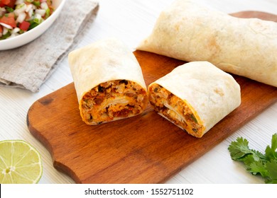 Homemade chorizo breakfast burritos on a rustic wooden board on a white wooden table, side view. Close-up.