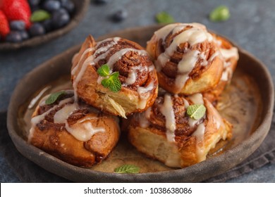 Homemade cinnamon buns in glaze on a dark plate with berries, dark background, copy space, top view.