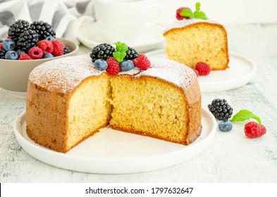 Pastel de esponja de vainilla o galleta casera, esparcidos con azúcar en polvo y bayas frescas sobre un plato blanco sobre un fondo de madera clara