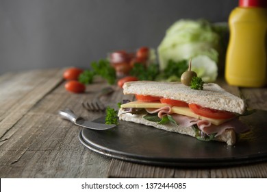 Homemade club sandwich. Toasted white bread triangles with ham, cheese fresh vegetables. Wooden table.