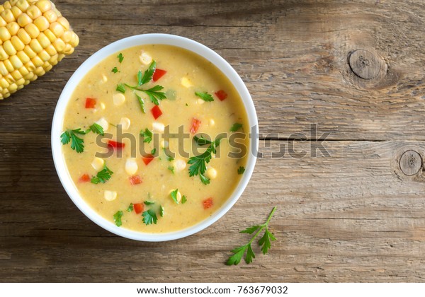 Homemade Corn Chowder Soup in\
white bowl. Vegetarian creamy corn soup with greens and\
vegetables.