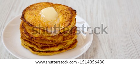 Homemade corn meal Johnny cakes with butter on a white plate over white wooden surface, side view. Space for text.
