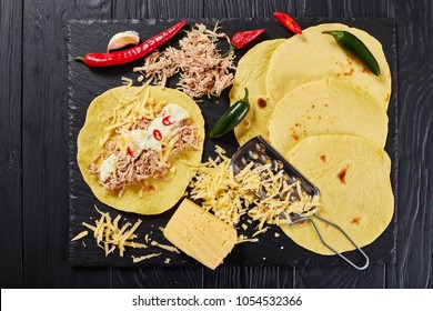 Homemade Corn Tortillas Layered With Shredded Meat, Sauce, Grated Cheese And Spices On Black Stone Board, On Wooden Table, View From Above, Close-up