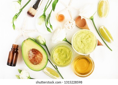 Homemade Cosmetic Mask With Fresh Avocado & Green Lime Slices Fruits, Ingredients On White Desktop, Jars With Essential Oil And Honey, Skincare & Hair Treatment. 