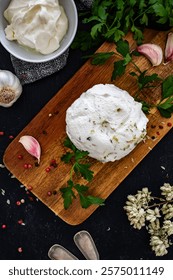 Homemade cottage cheese for spreading with garlic and oregano on cutting board on black table