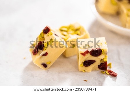 Homemade cranberry pistachio fudge square pieces on a kitchen counter.