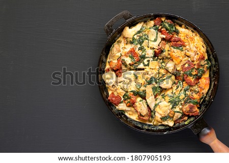 Homemade Creamy Tuscan Chicken in a cast-iron pan on black background, top view. Flat lay, overhead, from above. Copy space.
