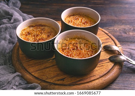Homemade creme brulee - traditional french vanilla cream dessert with caramelised brown sugar on top in black baking dishes, wooden plate and table. 