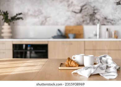 homemade croissant and cups of coffee on bamboo tray near striped towel from cotton material on wood tabletop on blurred kitchen background - Powered by Shutterstock