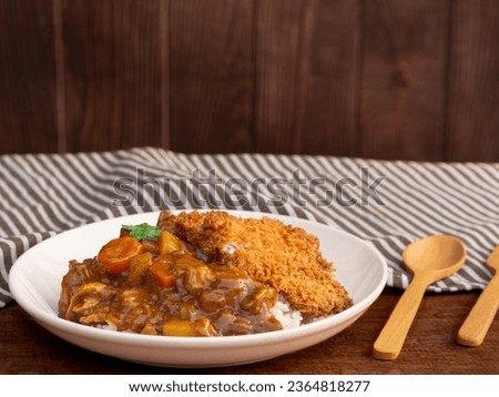 Homemade curry rice with crispy fried pork in white plate on wooden table background. Tonkatsu curry
