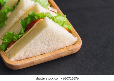 Homemade delicious sandwich ham cheese with lettuce and tomato in triangle shape on wood plate served with fresh orange juice on granite table with copy space for breakfast. 