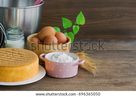 Homemade delicious sponge cake or soft cake on white plate with ingredients: eggs flour milk put on wood table with copy space. Bakery concept for background or wallpaper.