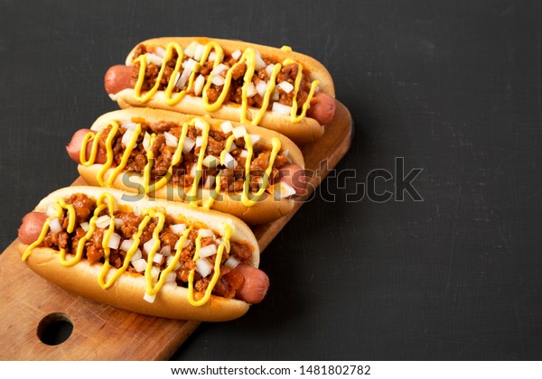 Homemade Detroit style\
chili dog on a rustic wooden board on a black surface, side view.\
Copy space.