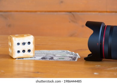 Homemade dice and dollar bills lie on a wooden table in front of a camera lens, photographers earnings