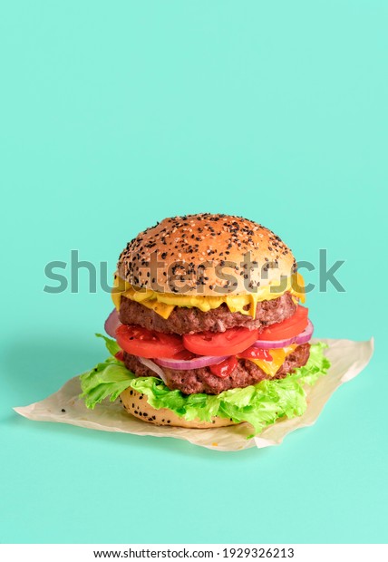 Homemade double burger minimalist on a green\
colored background. Vertical image with a juicy and delicious\
cheeseburger packed up with wax\
paper.